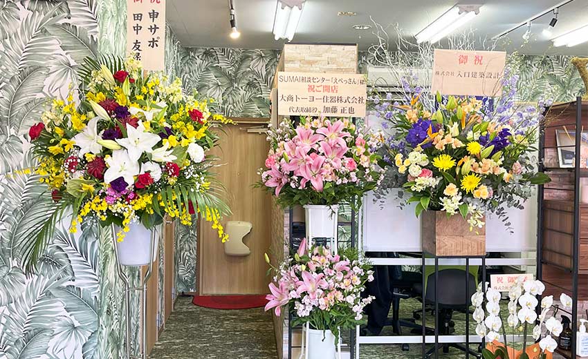 SUMAI相談センターえべっさん事務所の中。椰子の葉の壁紙が南国な印象。沢山の業者様からのスタンドお花でお祝い。